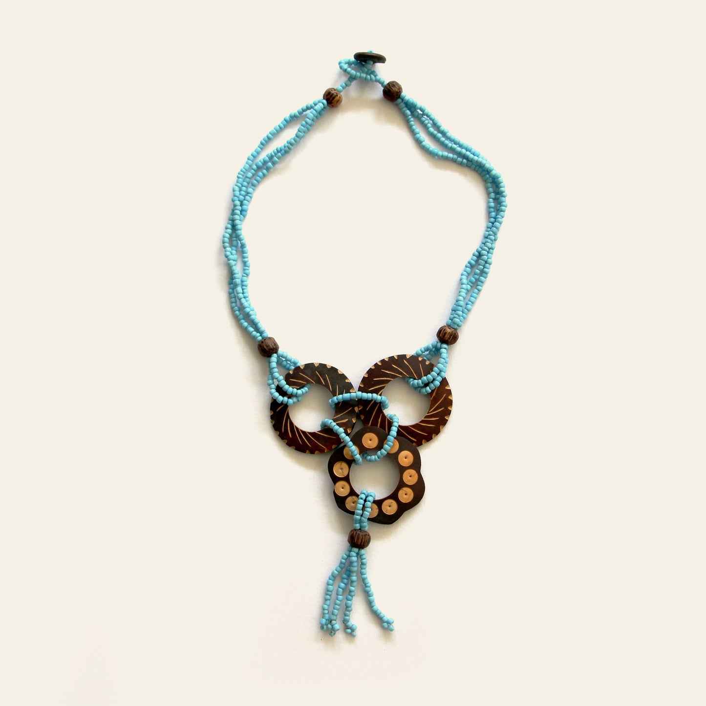 Handmade necklace featuring Turquoise seed beads and carved coconut shell loops linked together with beaded knots, finished with a tasseled drop — by Nayabijou.