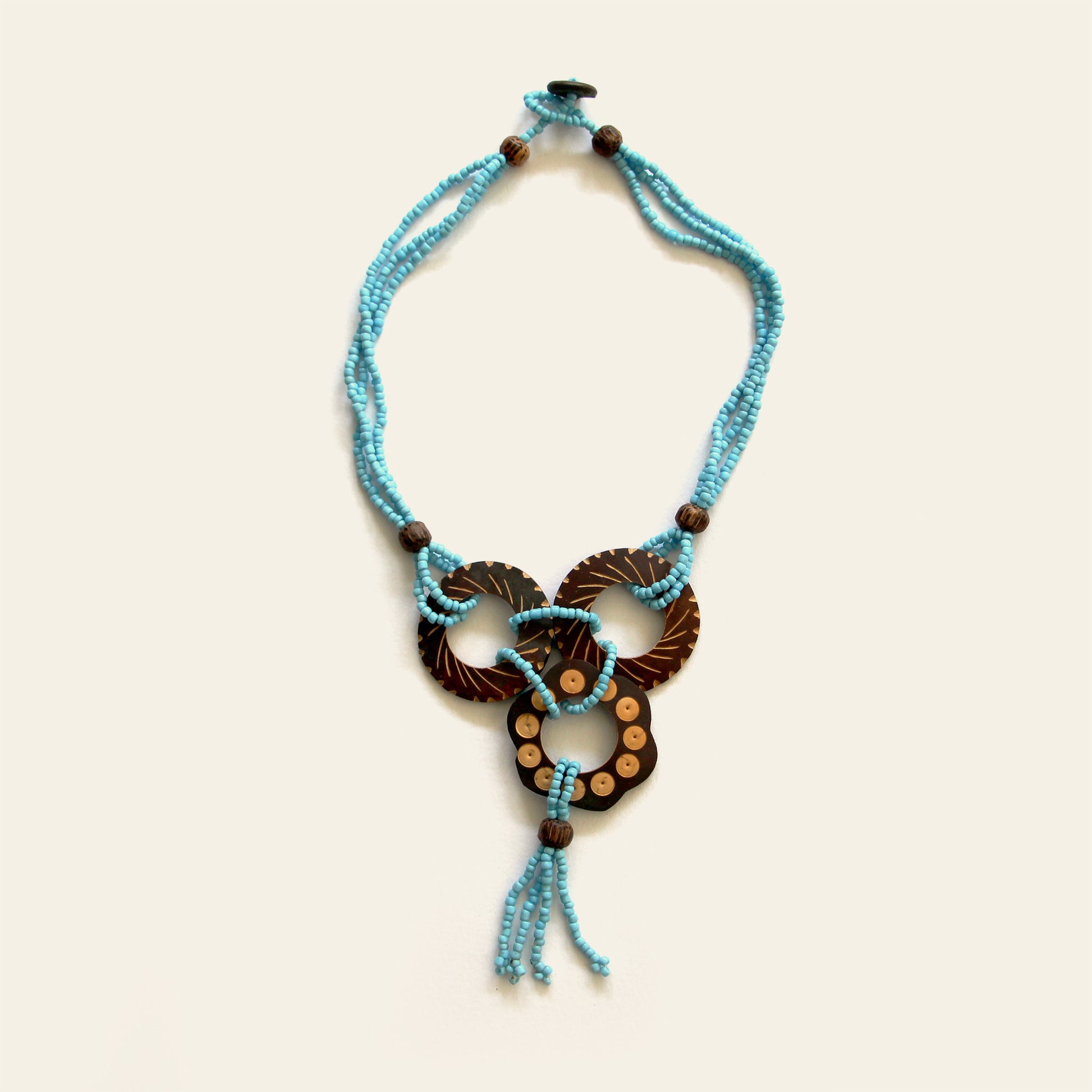 Handmade necklace featuring Turquoise seed beads and carved coconut shell loops linked together with beaded knots, finished with a tasseled drop — by Nayabijou.