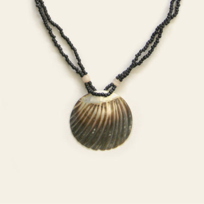 Closeup of handmade necklace with black seed beads and a dark scallop shell pendant – Nayabijou.