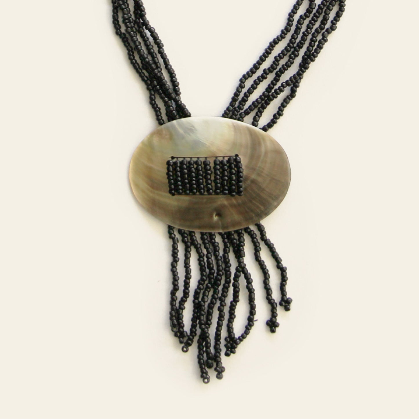 Close-up of oval shell pendant with threaded black seed beads and fringe strands – Nayabijou.