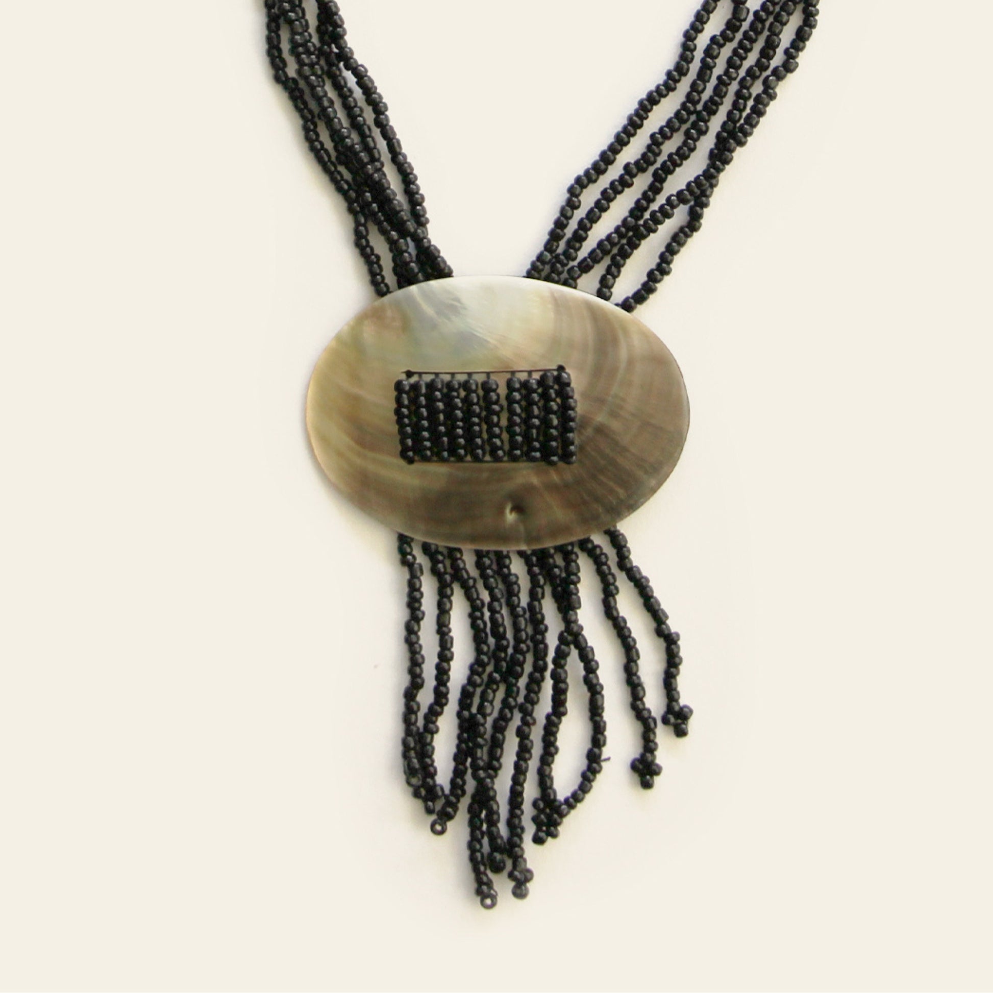 Close-up of oval shell pendant with threaded black seed beads and fringe strands – Nayabijou.