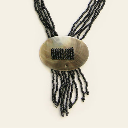 Close-up of oval shell pendant with threaded black seed beads and fringe strands – Nayabijou.