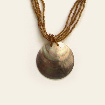 Close-up of round mother-of-pearl pendant with amber beaded strands