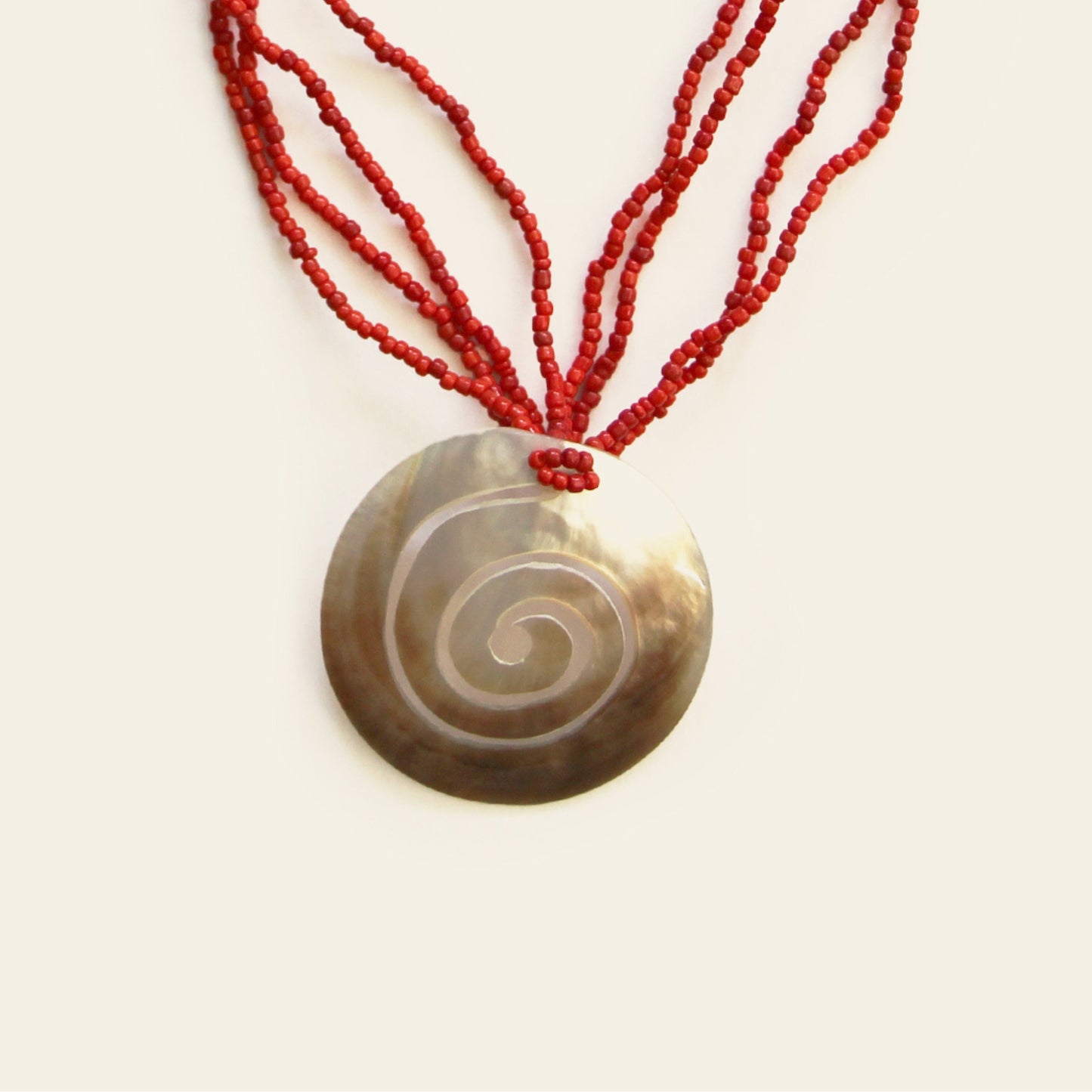 Close-up of spiral-engraved mother-of-pearl pendant with red seed bead strands – Nayabijou.