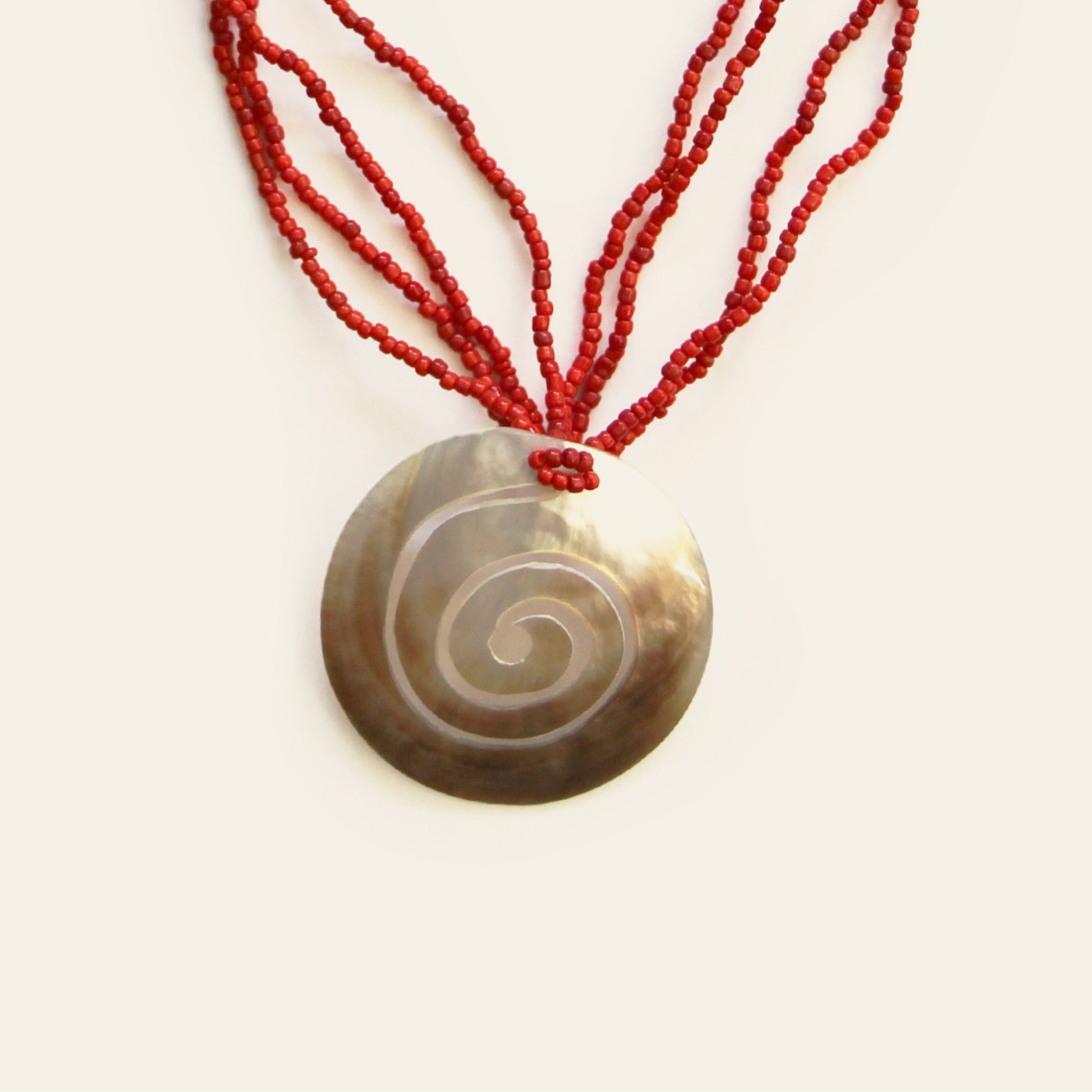 Close-up of spiral-engraved mother-of-pearl pendant with red seed bead strands – Nayabijou.
