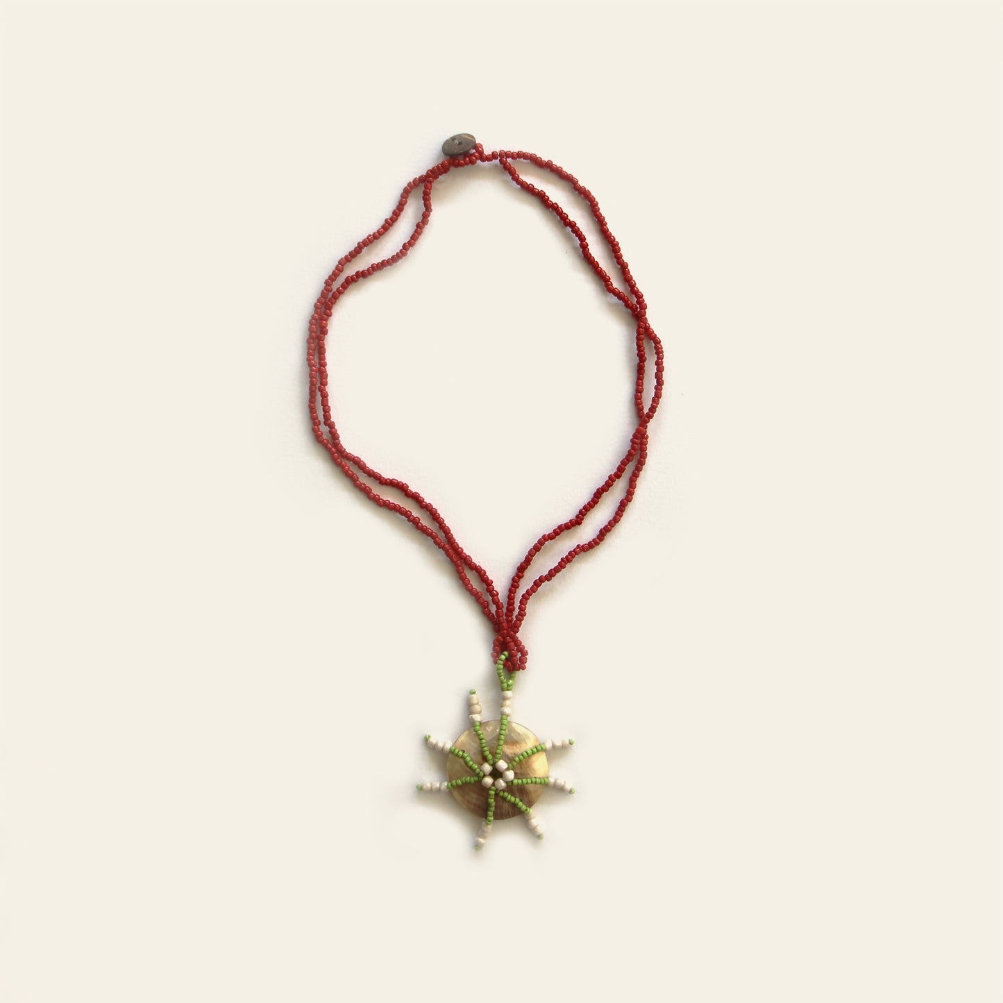 Full view of Starburst Shell Necklace with red beads and round mother of pearl pendant