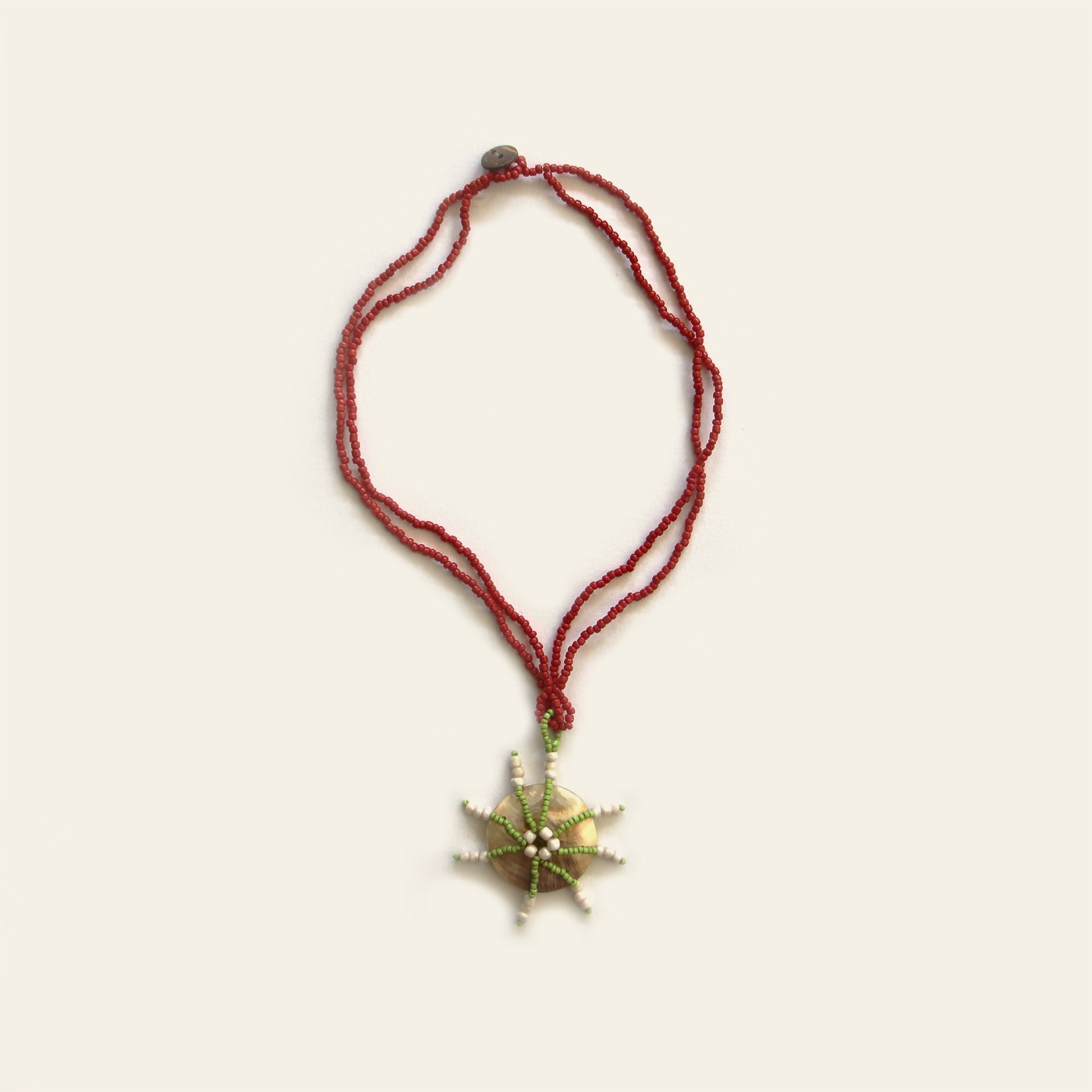 Full view of Starburst Shell Necklace with red beads and round mother of pearl pendant