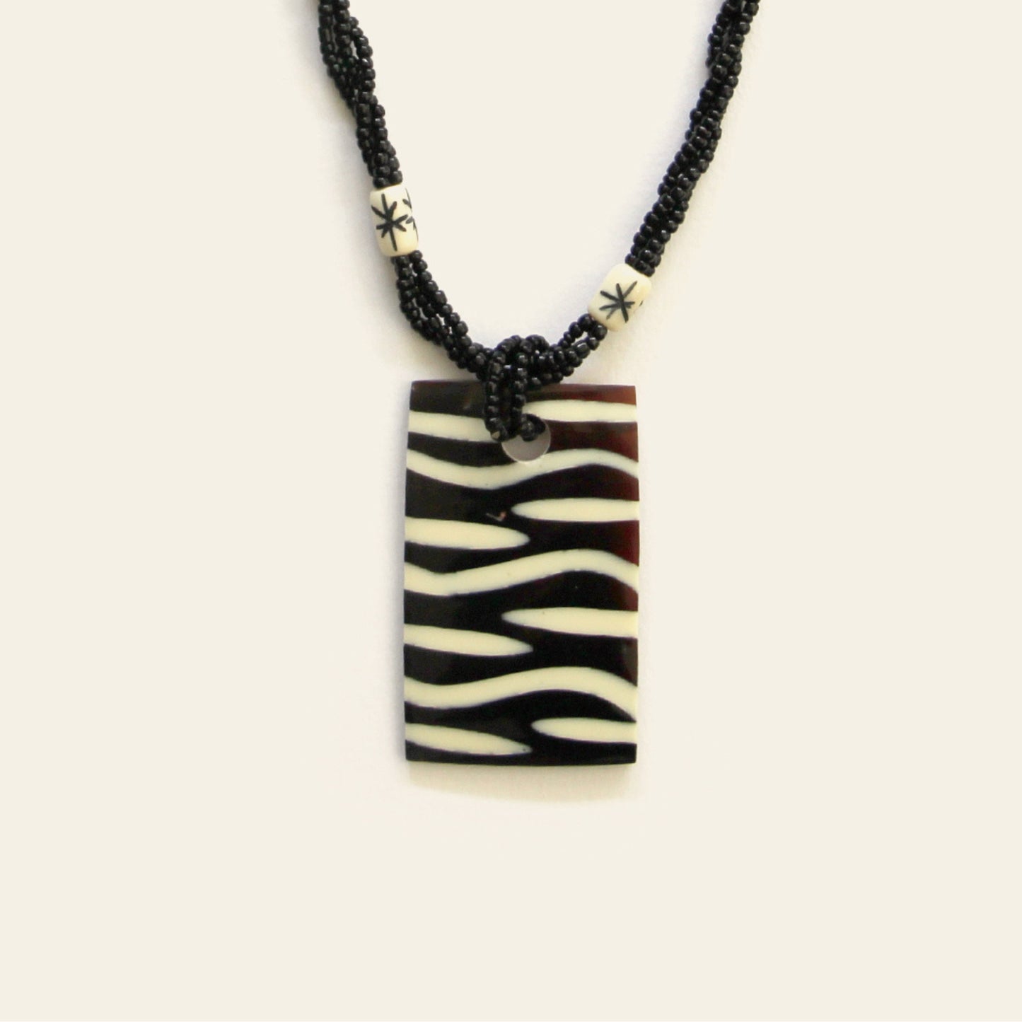 Closeup of rectangular zebra-pattern pendant necklace with black seed beads – Nayabijou.